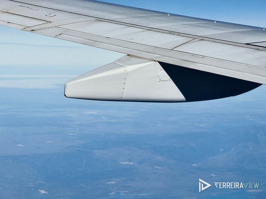 Asa de avião em pleno voo, com a terra lá em baixo