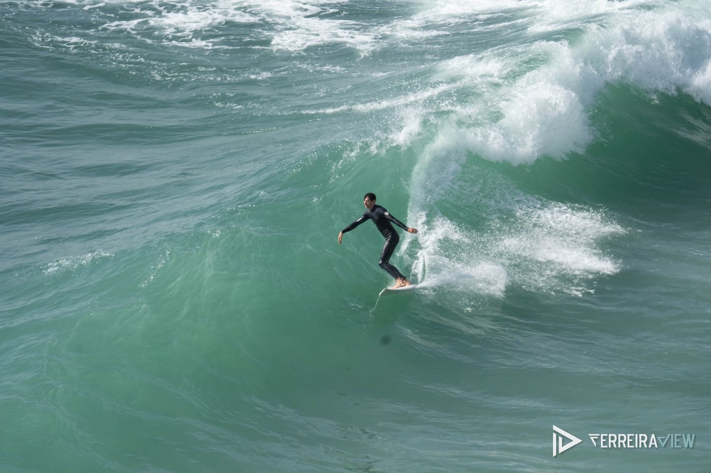 Surfista na parede de uma onda verde na Ericeira, fotografado com teleobjetiva
